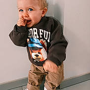 Diego a rejoint le concours — aidez-le/la à gagner de superbes lots ! toddler, child, blue_eyes, curly_hair, sweatshirt, teddy_bear_print, corduroy_pants, white_sneakers, indoor, floor_tiles, wall, standing, cute, playful, smiling, person, baby, fashion, casual, portrait