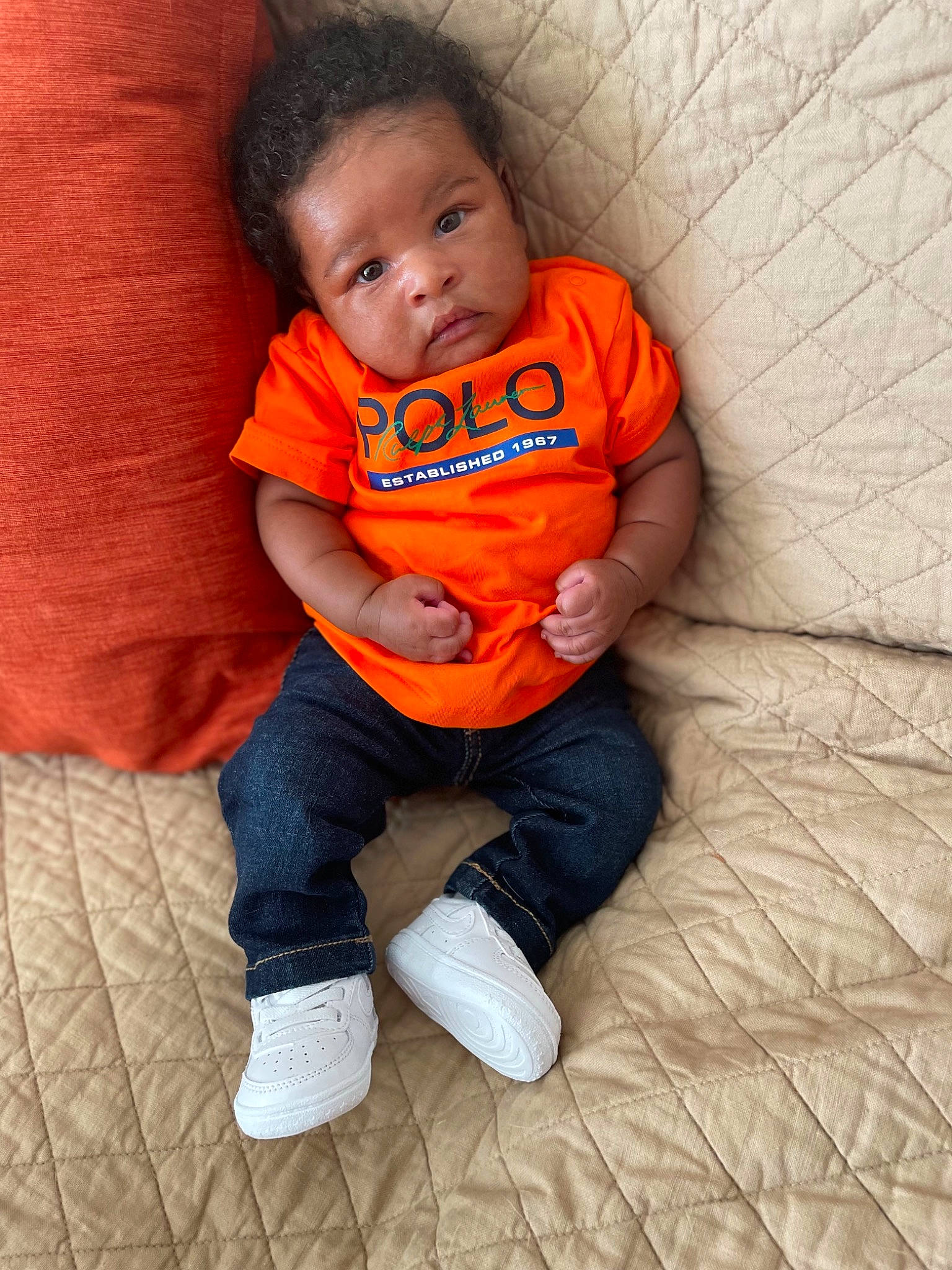 Azarias is registered to the contest to win money with this photo: arm, baby, baby_toddler_clothing, cheek, comfort, eye, face, finger, floor, flooring, head, leg, mouth, nose, orange, person, skin, sleeve, t_shirt, toddler