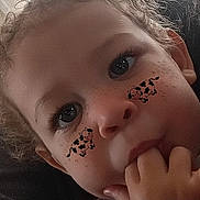 Harmony is registered to the contest to win money with this photo: child, face, close_up, curly_hair, finger_in_mouth, freckles, eyes, cartoon_stickers, cow_sticker, cute, innocent, portrait, skin, expression, playful, young, person, indoor, natural_light, freckled_face