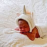 newborn, baby, sleeping, blanket, knitted_hat, unicorn, horn, pink_ears, white_bedspread, soft_texture, cozy, resting, infant, cute, portrait, indoors, peaceful, sleep, wrapped, child