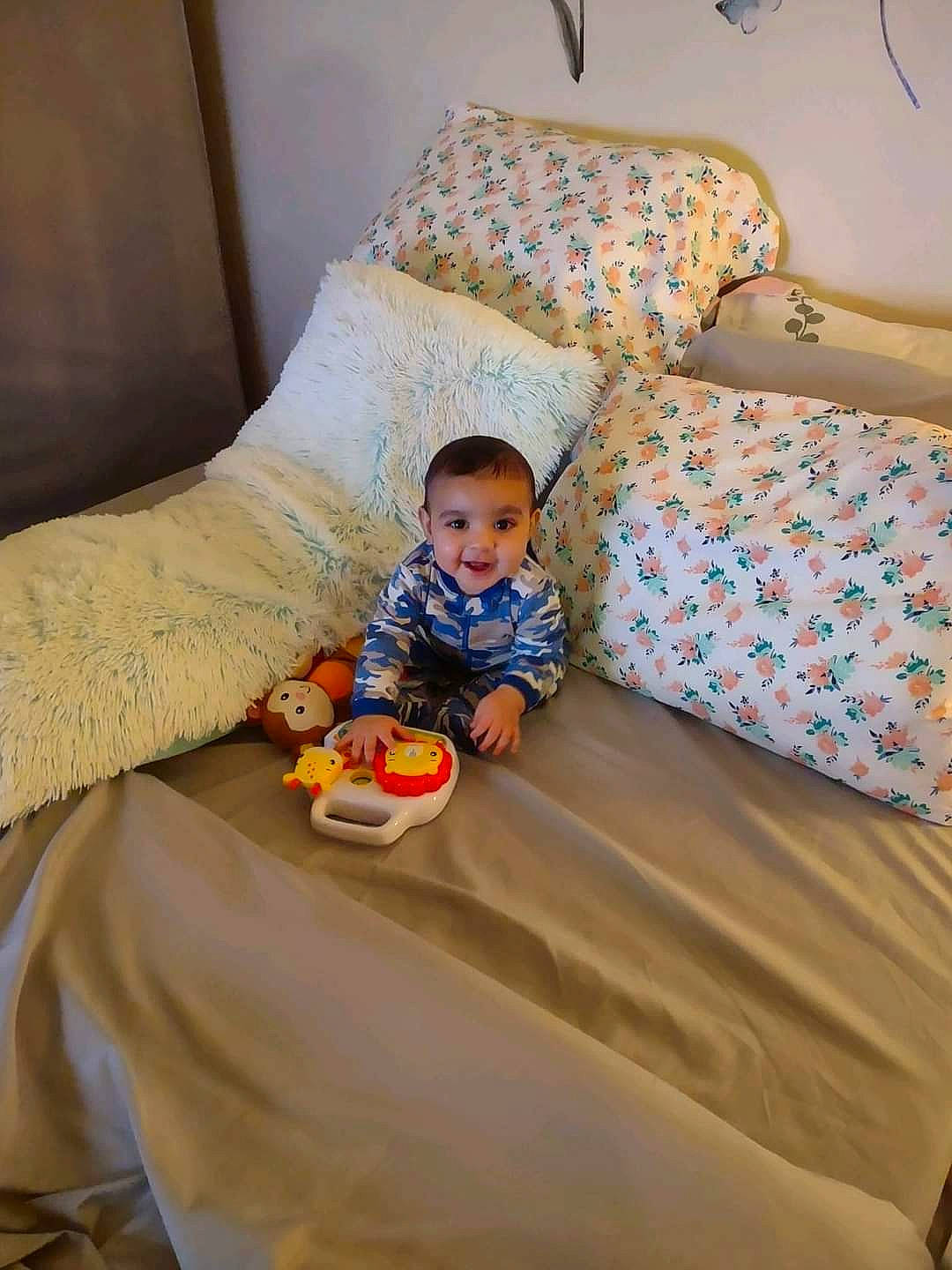 Gregory is registered to the contest to win money with this photo: baby, bed_sheet, bedding, child, comfort, couch, floor, flooring, head, joy, leisure, linens, orange, person, pillow, room, sitting, t_shirt, textile, throw_pillow