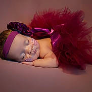Alexandria is registered to the contest to win money with this photo: baby, sleeping, tutu, headband, flower, nasal_cannula, medical_tape, infant, portrait, soft_lighting, maroon, peaceful, resting, newborn, cute, closeup, child, studio_photo, pink_background, adorable