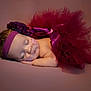 baby, sleeping, tutu, headband, flower, nasal_cannula, medical_tape, infant, portrait, soft_lighting, maroon, peaceful, resting, newborn, cute, closeup, child, studio_photo, pink_background, adorable