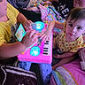 Liliana is registered to the contest to win money with this photo: child, baby, adult, toy, keyboard, playing, blanket, pillow, glowing, colorful, indoor, family, curious, smiling, glasses, sitting, clothing, person, cute, interaction