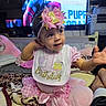 Liliana is registered to the contest to win money with this photo: baby, child, birthday, pink, bow, bib, blanket, plush_toy, television, indoor, smiling, cute, clothing, headband, person, celebration, first_birthday, toddler, happy, room