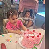child, birthday_cake, hello_kitty, pink_cake, cherries, candle, stroller, table, party, smiling, baby, high_chair, indoor, celebration, chairs, person, happy, toy, clothing, hair_clip