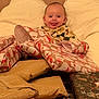 Hudson is registered to the contest to win money with this photo: baby, child, present, gift, wrapping_paper, cushion, pillow, smile, tongue, indoor, cozy, holiday, celebration, face, person, cute, happy, sitting, clothing, patterned