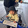 adult, baby, bucket_hat, candid, cozy_jacket, floor, hands, ikea_sign, infant_seat, jeans, looking_at_camera, metal_cart, pacifier, pacifier_clip, portrait, retail_store, shopping, shopping_cart, socks, window