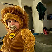 Dexter is registered to the contest to win money with this photo: toddler, child, lion_costume, pacifier, indoor, living_room, couch, furry, cute, costume, baby, soft, plush, portrait, face, expression, home, clothing, seated, young