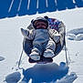 baby, snow, snowsuit, baby_chair, outdoor, winter, sunlight, shadow, fence, cold, cozy, floral_pattern, child, warm_clothing, footwear, hat, mittens, playful, cute, relaxing