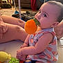 Espyn is registered to the contest to win money with this photo: baby, child, toy, plush_toy, sitting, indoor, floor, person, legs, hand, clothing, patterned_clothing, orange, green, blue, face, chewing, playtime, living_room, carpet