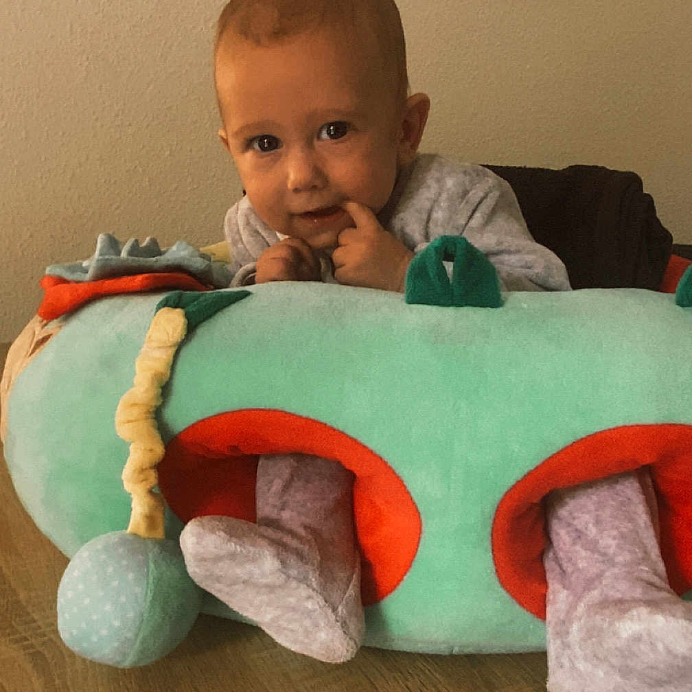 Ezelyo participe au concours pour gagner de l'argent avec cette photo : artwork, baby, child, clothing, colorful, curious, cute, face, feet, furniture, indoor, infant, person, play, plush_toy, smile, table, toy, wall, wood