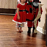 Zayah is registered to the contest to win money with this photo: barefoot, cabinet, child, christmas, decor, festive, figure, flooring, girl, holiday, indoor, list, person, red_clothing, santa_dress, santa_hat, smiling, toy, wall, wooden_floor