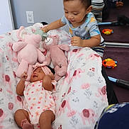 Rosalyn is registered to the contest to win money with this photo: baby, toddler, stuffed_animals, blanket, mirror, toys, floor, child, indoor, sleeping, pink, pattern, clothing, interaction, soft_toys, smiling, headband, person, cute, family