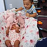 baby, toddler, stuffed_animals, blanket, mirror, toys, floor, child, indoor, sleeping, pink, pattern, clothing, interaction, soft_toys, smiling, headband, person, cute, family
