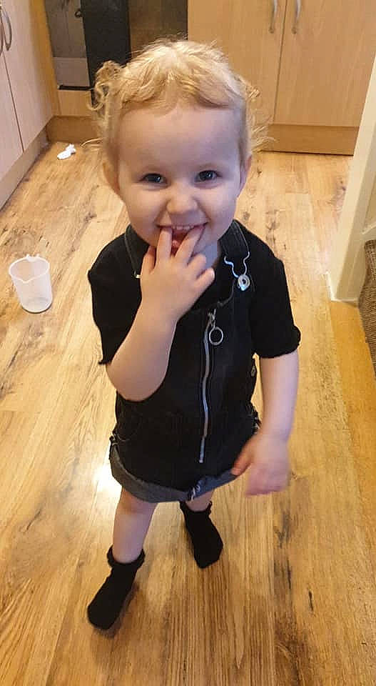 Mckenna-mae Grace is registered to the contest to win money with this photo: baby_toddler_clothing, cheek, chin, eye, face, facial_expression, floor, flooring, head, iris, leg, nose, person, skin, sleeve, smile, standing, thumb, toddler, white