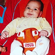 Lilie participe au concours pour gagner de l'argent avec cette photo : baby, infant, smile, fisher_price, baby_seat, red, orange, yellow_clothing, white_socks, hand, face, child, cute, indoor, toy, seat_belt, plush, comfort, young_child, portrait