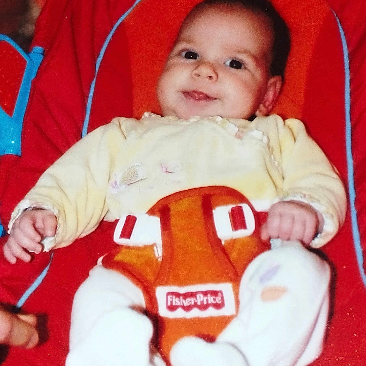 Lilie participe au concours pour gagner de l'argent avec cette photo : baby, baby_seat, child, comfort, cute, face, fisher_price, hand, indoor, infant, orange, plush, portrait, red, seat_belt, smile, toy, white_socks, yellow_clothing, young_child