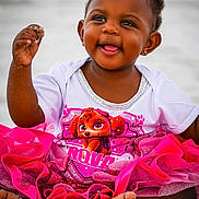 Nova joined the competition — help win amazing prizes! toddler, child, smiling, sand, beach, pink_tutu, white_shirt, cartoon_character, happy, barefoot, cute, playful, outdoor, summer, portrait, sitting, dark_skin, short_hair, earrings, fun