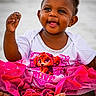 toddler, child, smiling, sand, beach, pink_tutu, white_shirt, cartoon_character, happy, barefoot, cute, playful, outdoor, summer, portrait, sitting, dark_skin, short_hair, earrings, fun