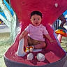 child, colorful, expression, fun, mouth, mushroom, orange, outdoor, park, pink, play, playground, sculpture, shirt, shorts, sitting, socks, teeth, toddler, tree