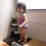 Xion is registered to the contest to win money with this photo: toddler, child, swimsuit, standing, indoor, window, sunlight, plant, greenery, wooden_surface, barefoot, hair, face, smile, corner, shadow, bright, colorful, room, casual
