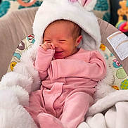 Aria is registered to the contest to win money with this photo: baby, infant, smile, pink_clothing, white_hat, blanket, baby_seat, soft_texture, cute, cozy, playful, child, indoors, warm, happy, newborn, face, hand, footed_pajamas, portrait