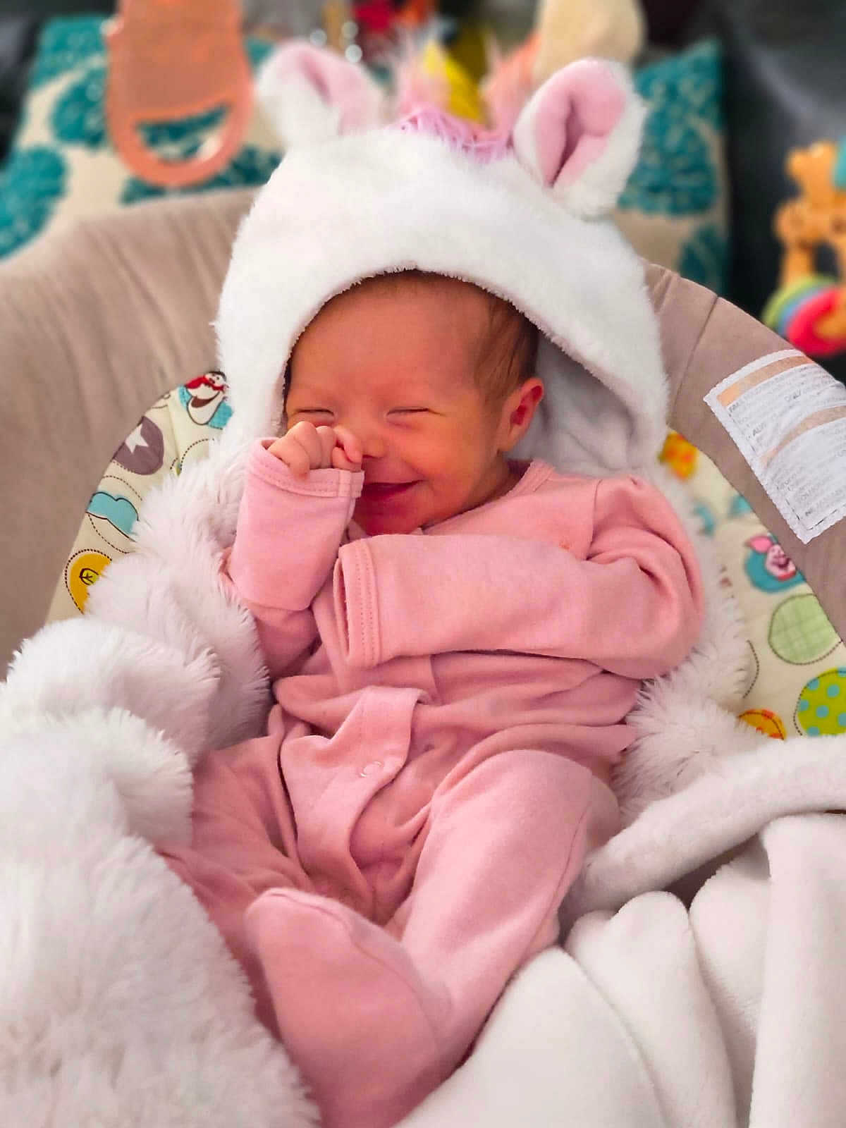 Aria is registered to the contest to win money with this photo: baby, infant, smile, pink_clothing, white_hat, blanket, baby_seat, soft_texture, cute, cozy, playful, child, indoors, warm, happy, newborn, face, hand, footed_pajamas, portrait