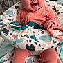 baby, infant, smiling, happy, toy, baby_seat, coral_clothing, patterned_fabric, hand, face, cute, child, indoor, baby_toys, seat, legs, footed_pajamas, colorful, cheerful, playful