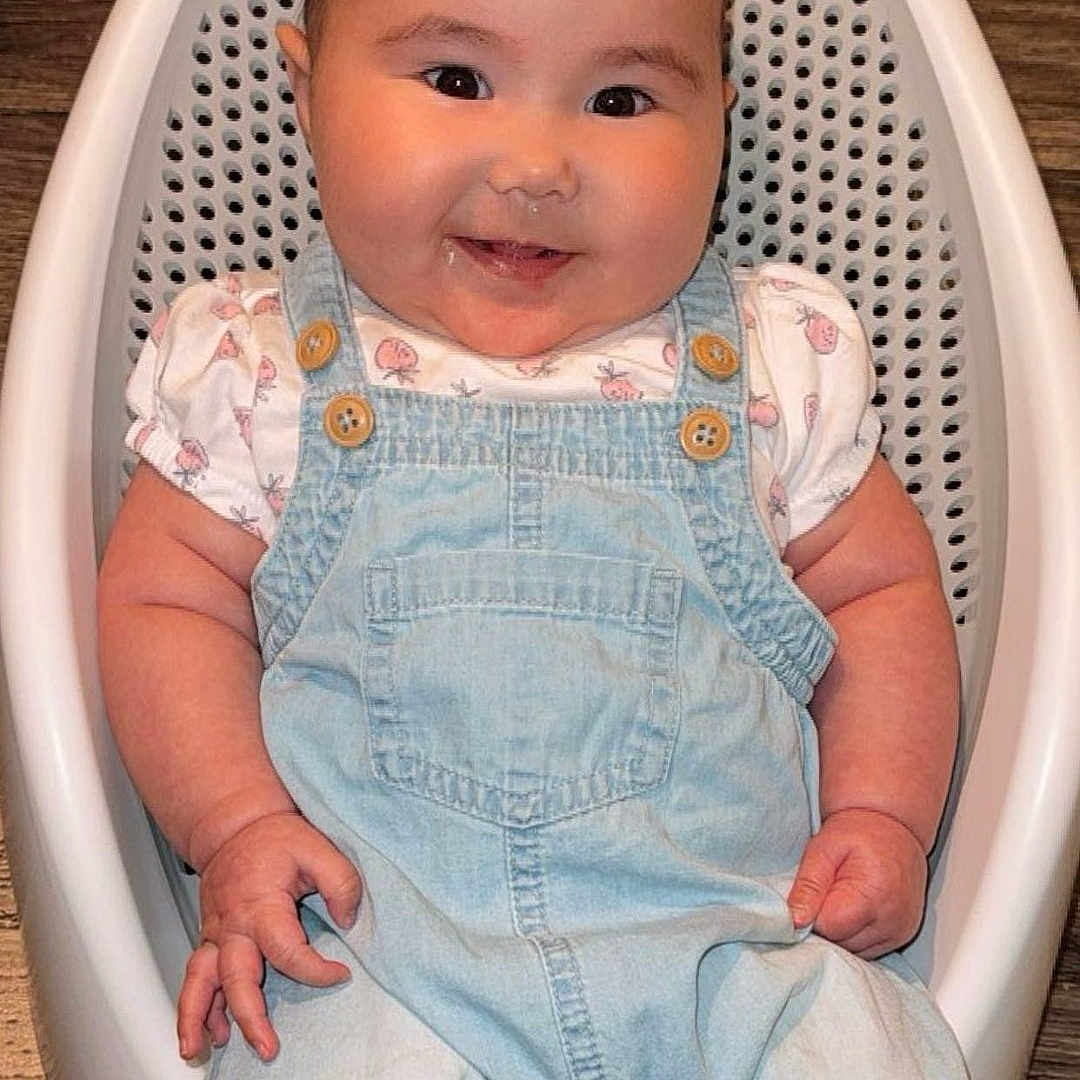 Lena-Sage is registered to the contest to win money with this photo: baby, baby_bath_seat, baby_toy, casual, child, chubby_cheeks, clothing, cute, denim_overalls, drool, face, footwear, happy, indoor, infant, person, sitting, smiling, white_shirt, wooden_floor