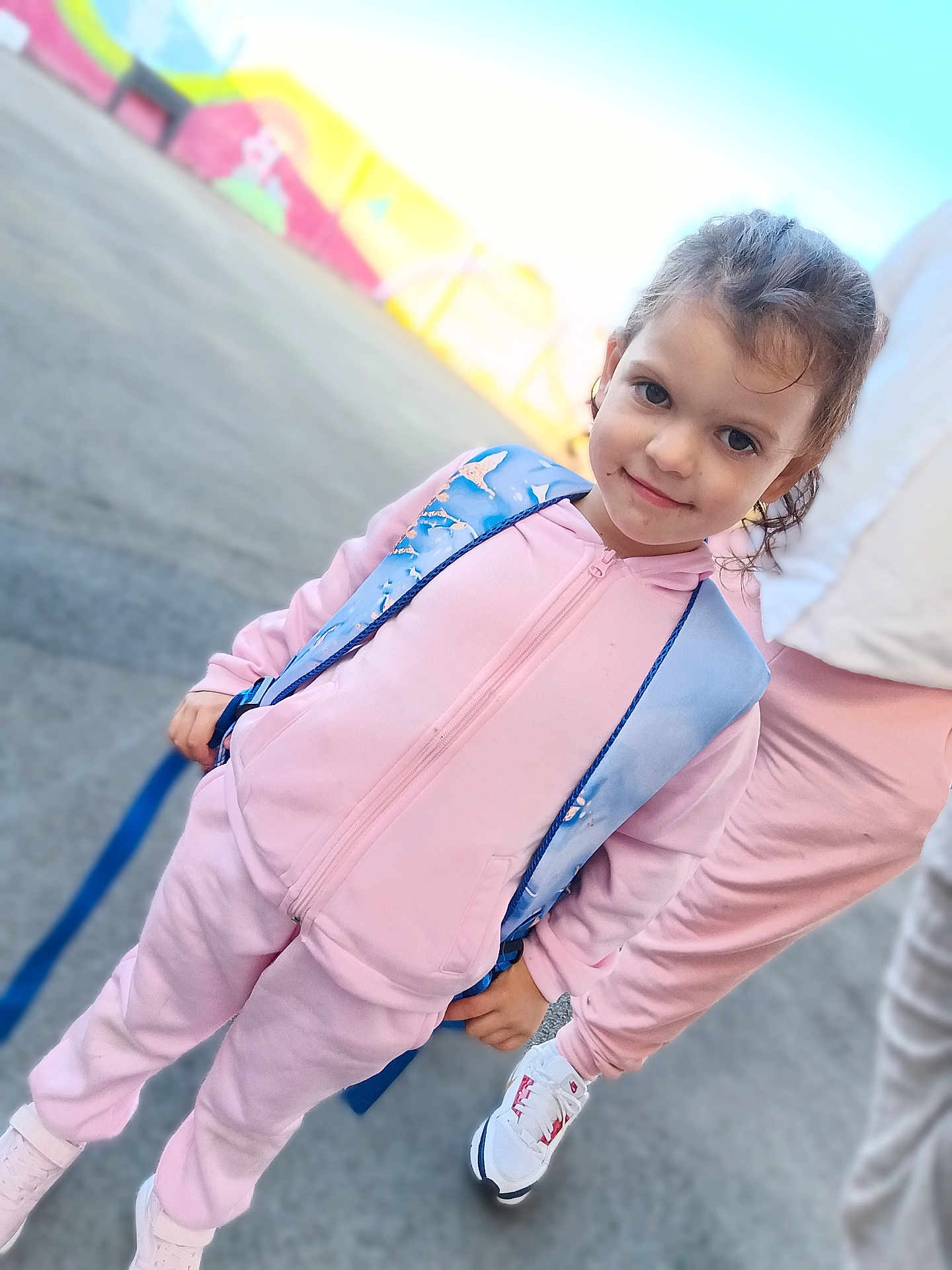 Talya participe au concours pour gagner de l'argent avec cette photo : child, girl, pink_tracksuit, blue_backpack, outdoor, smiling, person, sneakers, concrete, mural, colorful, casual_clothing, young, standing, happy, daylight, hair_tied, urban, playful, cute