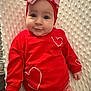 baby, infant, red_clothing, headband, bow, heart_pattern, blanket, cute, child, smiling, lying_down, soft_texture, indoors, portrait, closeup, adorable, warm_colors, baby_fashion, toddler, happy