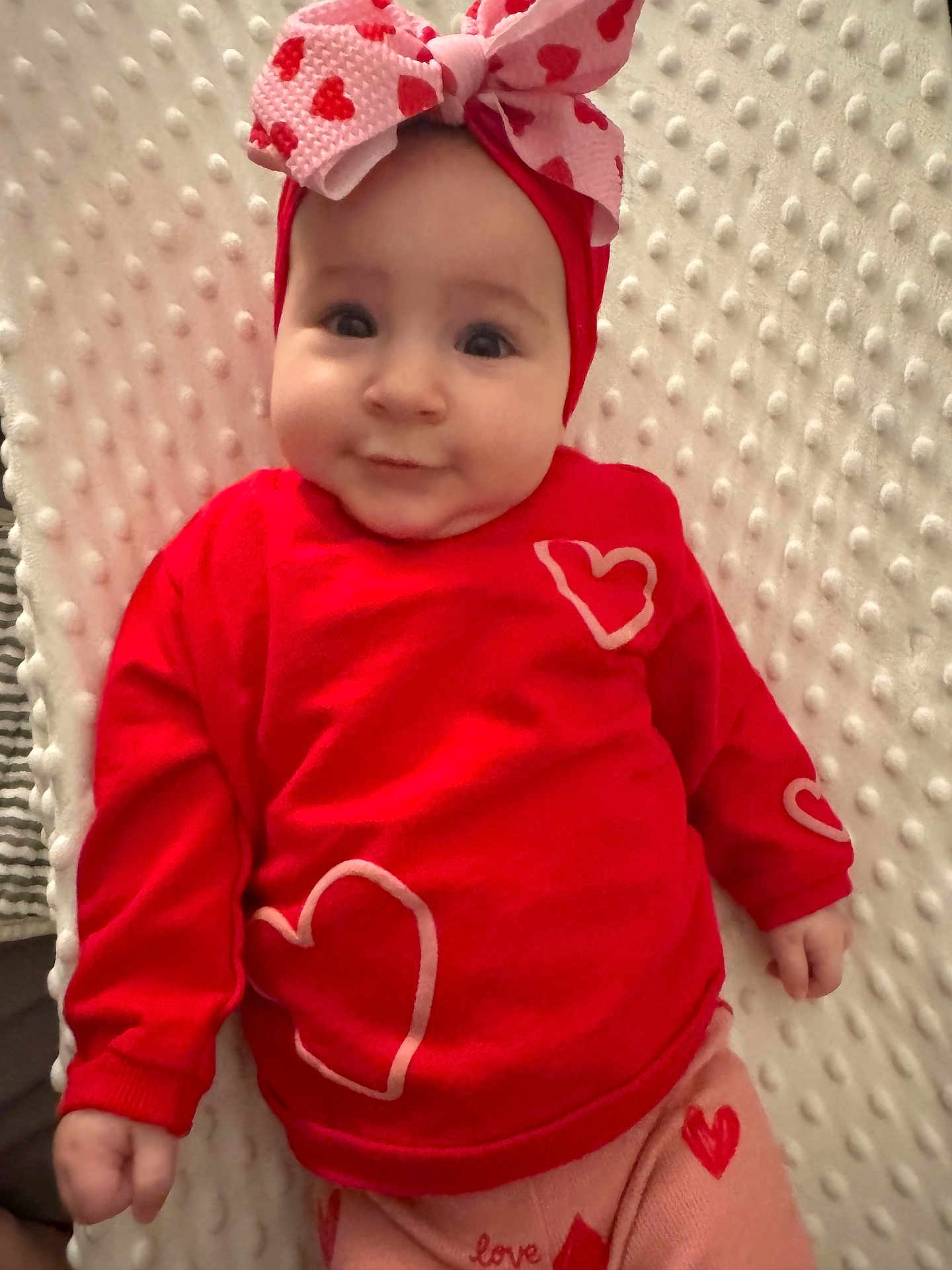 Lilianna is registered to the contest to win money with this photo: baby, infant, red_clothing, headband, bow, heart_pattern, blanket, cute, child, smiling, lying_down, soft_texture, indoors, portrait, closeup, adorable, warm_colors, baby_fashion, toddler, happy