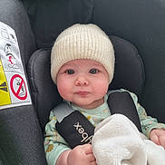 Laïa participe au concours pour gagner de l'argent avec cette photo : baby, infant, car_seat, blanket, knit_hat, onesie, child, face, seatbelt, safety, cute, indoors, soft_texture, comfort, expression, young_child, protection, car, person, candid