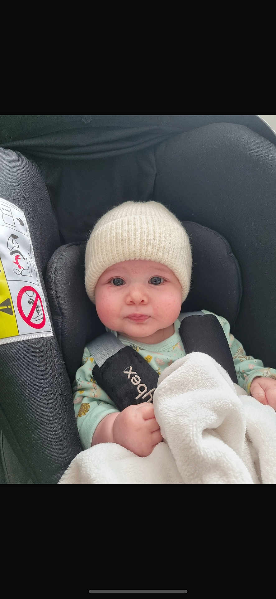Laïa participe au concours pour gagner de l'argent avec cette photo : baby, infant, car_seat, blanket, knit_hat, onesie, child, face, seatbelt, safety, cute, indoors, soft_texture, comfort, expression, young_child, protection, car, person, candid
