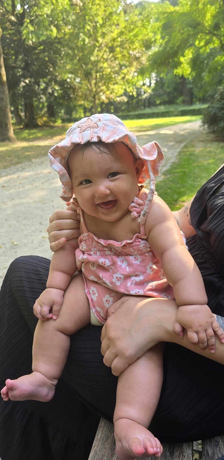 Mai Linh participe au concours pour gagner de l'argent avec cette photo : baby, child, smiling, pink_hat, pink_clothing, outdoor, nature, greenery, person, happy, infant, sunlight, park, grass, trees, bench, holding, cute, summer, portrait