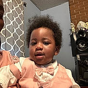 Prince is registered to the contest to win money with this photo: baby, bow_tie, child, clothing, curly_hair, curtains, cute, face, fashion, happy, home, indoor, person, pink_vest, portrait, smiling, speaker, toddler, trophies, young