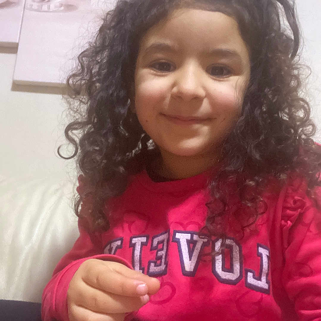 Raissa a rejoint le concours — aidez-le/la à gagner de superbes lots ! child, clothing, couch, cozy, curly_hair, eyes, face, girl, hair, hand, happy, heart_pattern, home_decor, indoor, pink_sweater, portrait, sitting, smile, sofa, wall_art