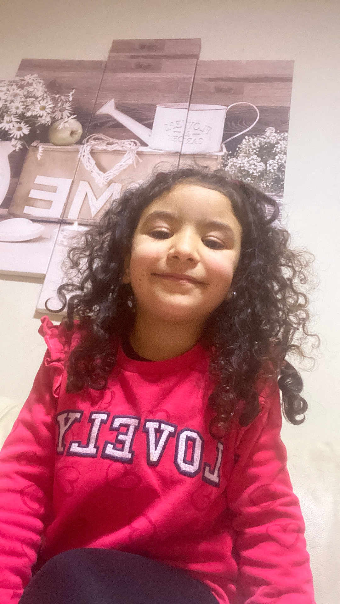 Raissa a rejoint le concours — aidez-le/la à gagner de superbes lots ! casual_clothing, child, cozy, curly_hair, decor, face, flowers, girl, happy, home, indoor, person, pink_sweatshirt, portrait, relaxed, selfie, sitting, smiling, wall_art, young
