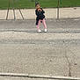 child, girl, outdoor, sports_field, fence, grass, mountains, cloudy_sky, snack, pink_leggings, black_top, pavement, people, playing, daytime, casual_clothing, activity, recreation, leisure, happy