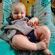 Cole is registered to the contest to win money with this photo: baby, infant, smile, blanket, toy, baby_seat, colorful, cute, legs, feet, clothing, indoor, child, face, playful, happy, comfort, seat, animal_print, relaxing