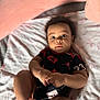 baby, infant, child, black_clothing, red_clothing, blanket, bed, lying_down, hands, feet, face, eyes, curious, indoors, soft_texture, cute, portrait, young, person, skin