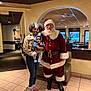 archway, baby, boots, celebration, child, clothing, family, furniture, glasses, holding, holiday, indoor, person, plant, restaurant, santa_claus, smile, tile_floor, wall, window