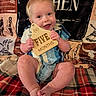 baby, infant, child, smiling, holding_object, wooden_sign, five_months, blue_eyes, blonde_hair, plaid_blanket, western_theme, cowboy, sitting, cute, portrait, clothing, shorts, happy, indoor, milestone