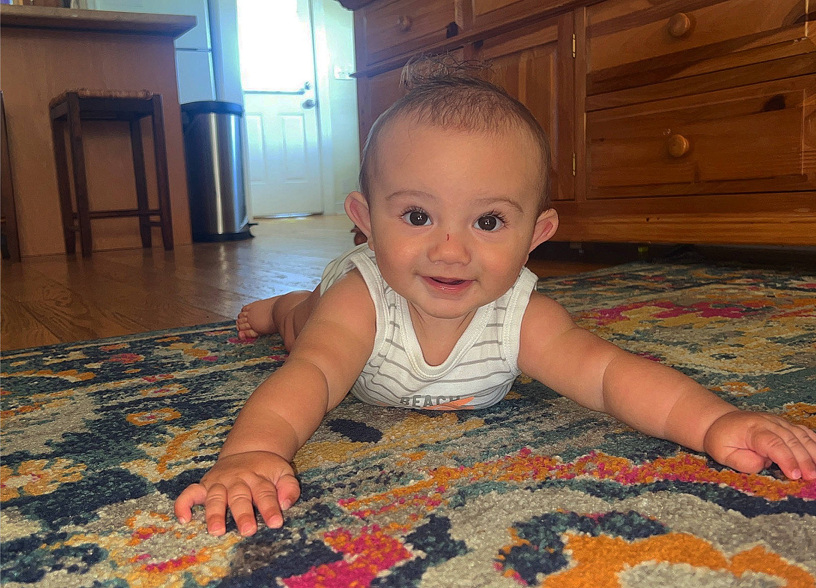 Lawson is registered to the contest to win money with this photo: baby, baby_toddler_clothing, black, brown, cabinetry, cheek, child, crawling, finger, floor, flooring, hardwood, iris, joy, people, person, skin, smile, standing, toddler