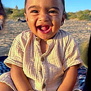 Kenzo is registered to the contest to win money with this photo: toddler, child, smiling, happy, outdoor, beach, sand, sunlight, buttoned_shirt, sitting, blanket, portrait, face, young_child, cute, natural_light, casual_clothing, daytime, skin, baby