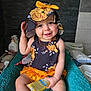 Ombelyne a rejoint le concours — aidez-le/la à gagner de superbes lots ! baby, child, smile, hat, floral_pattern, yellow, orange, towel, bathroom, lotion, cute, sitting, skin, person, infant, playful, clothing, accessory, happy, young