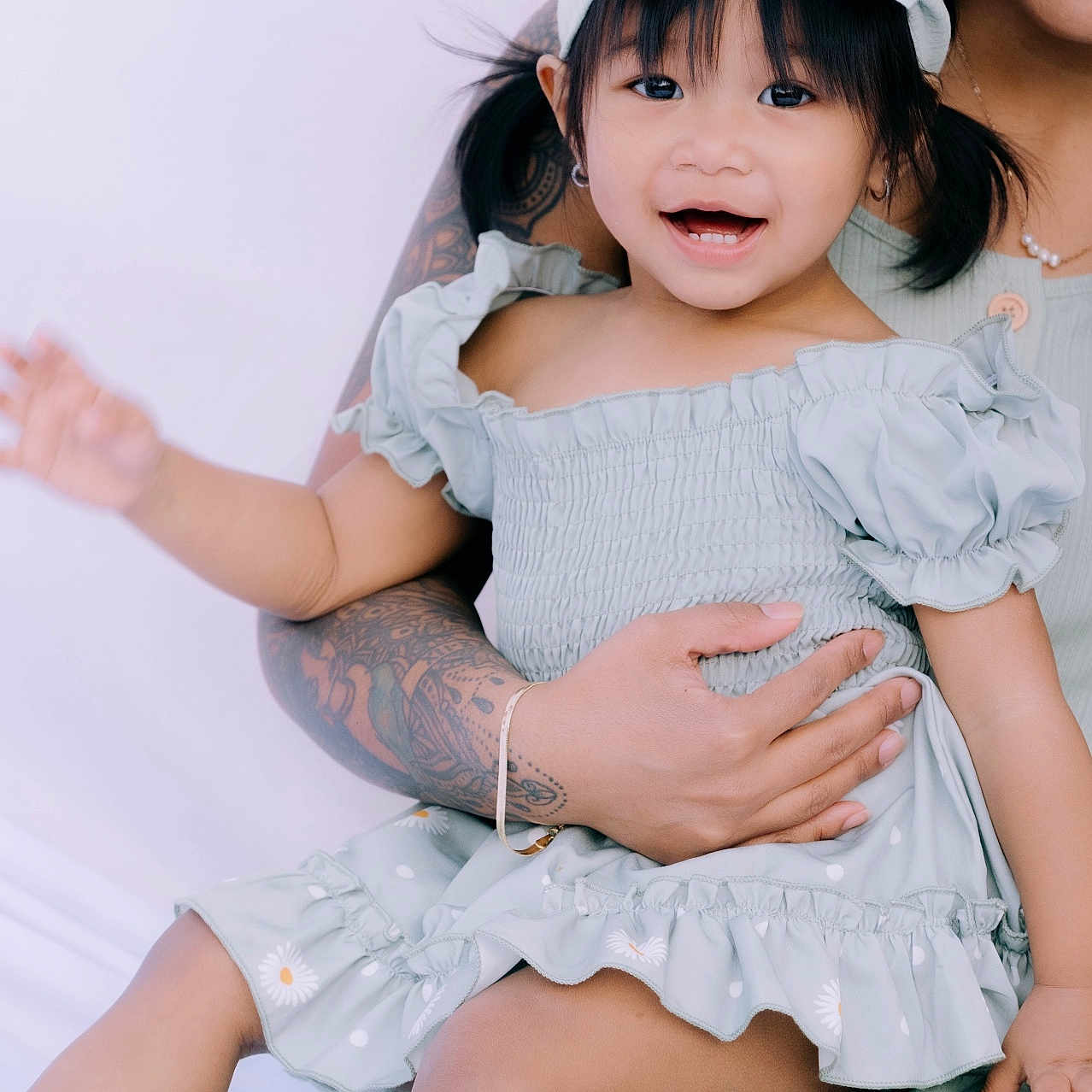 Jade is registered to the contest to win money with this photo: adult, arm, bow, child, cute, dress, face, fashion, hand, happy, holding, indoor, joyful, person, portrait, sitting, skin, smiling, tattoo, toddler