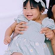 Jade is registered to the contest to win money with this photo: child, toddler, smile, happy, dress, bow, headband, flower_pattern, pigtails, person, hand, holding, cute, innocence, portrait, baby, skin, clothing, joy, light_background