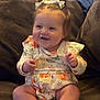 baby, child, smiling, sitting, pigtails, bow, pumpkin, outfit, couch, indoor, happy, cute, infant, clothing, person, feet, hands, face, hair, home